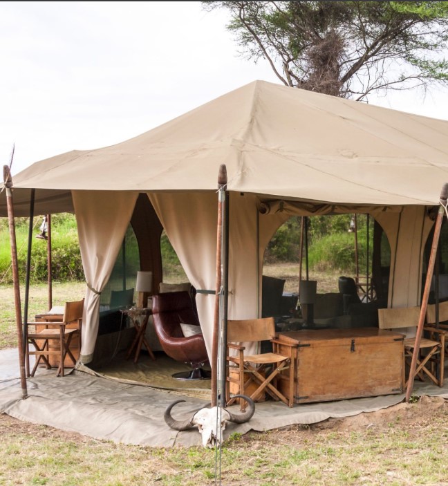 Luxury tented camp in Serengeti with sunrise over savannah and safari chairs on the veranda.