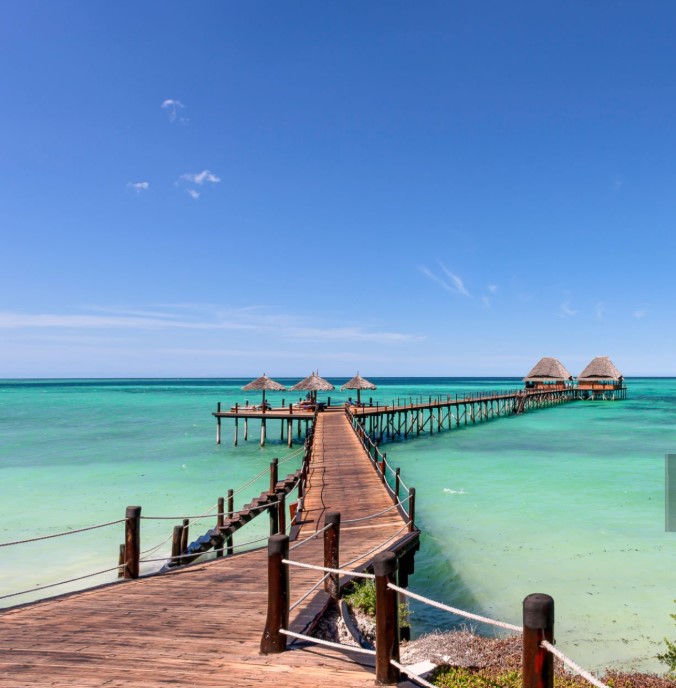 A stunning view of Zanzibar’s beach with clear turquoise waters, palm trees, and blue skies, perfect for a getaway.